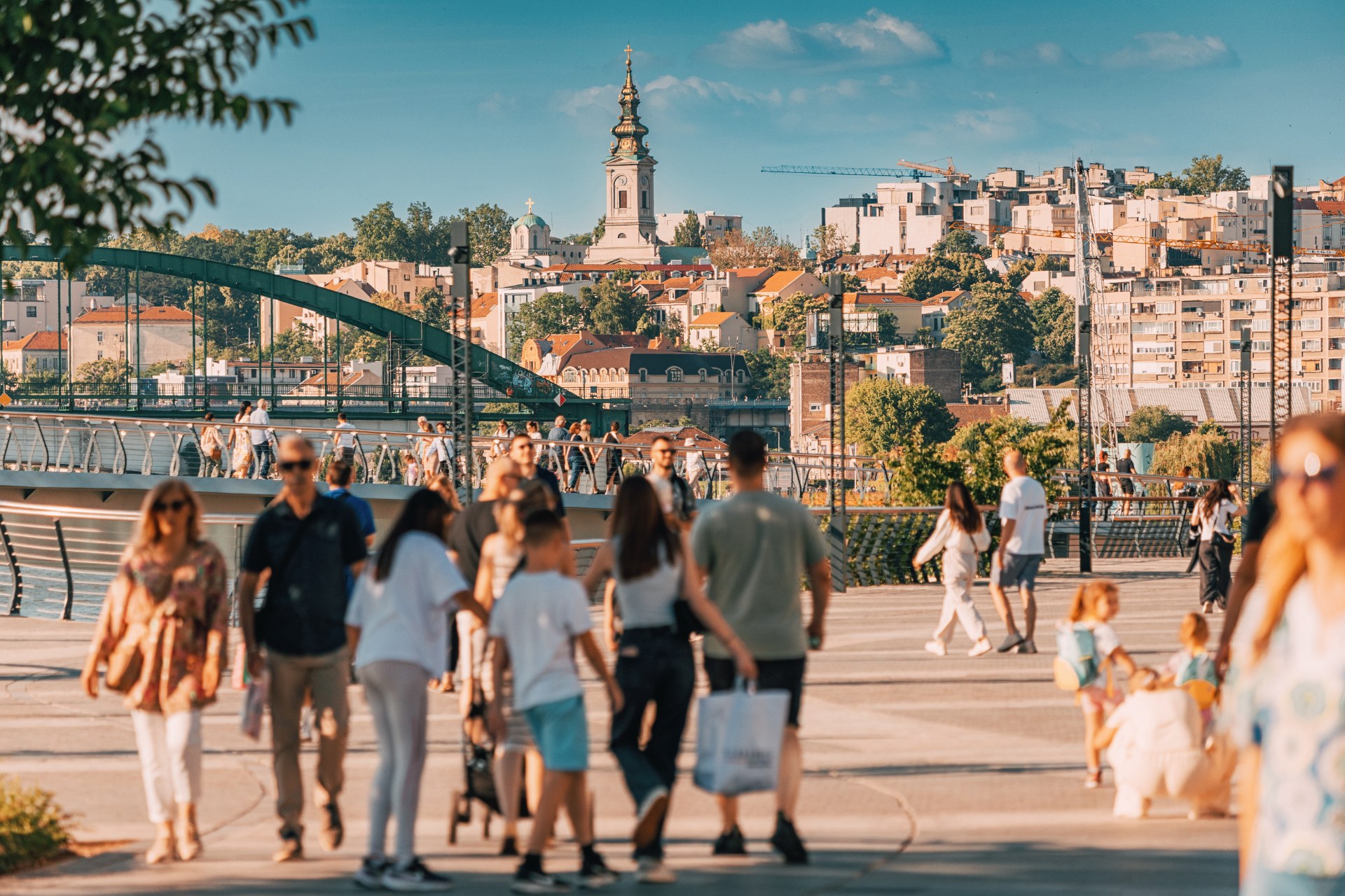 Des promeneurs sur la promenade de la Save à Belgrade, avec la vieille ville et un clocher en arrière-plan